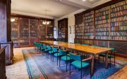 A grand historical meeting room with a long wooden table and bookcases.