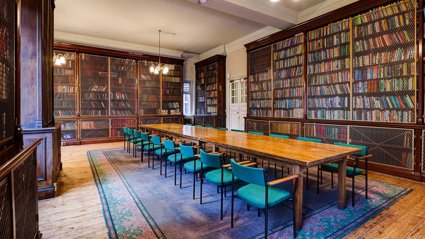 A grand historical meeting room with a long wooden table and bookcases.