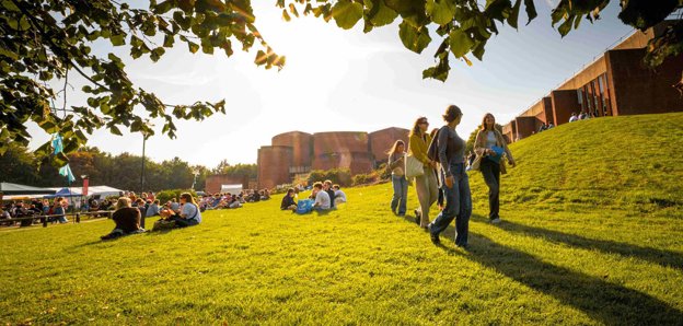University of Sussex campus showing buildings and students sitting and walking on the grass.