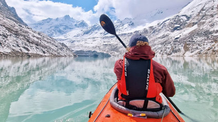 A kayaker approaches a glacier front in a Nepalese mountain landscape.