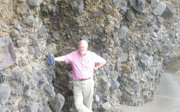 Murray Gray in pink shirt and khaki trousers standing next to a rock face.