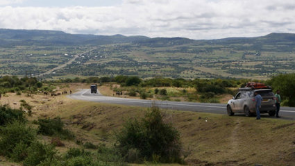 Car parked on a winding road, with herds of cows walking beside the road and a large expanse of open land in the distance.
