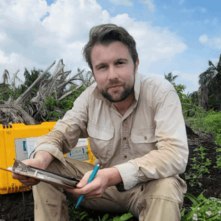 Dr Thomas Smith sitting in a field, holding a pen and clipboard.