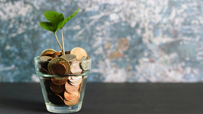 A glass jar containing coins with a small plant growing out of the top.