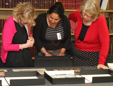 Three people looking at archived Collection item in a library.