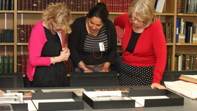 Three people looking at archived Collection item in a library.