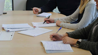 Students sitting on a table and writing on sheets of paper.