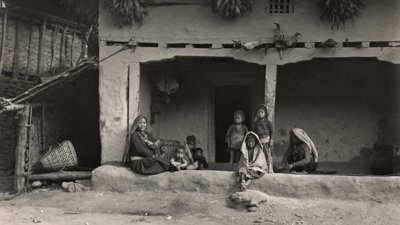 Black and white image of adults and children sat outside a typical Limbu house in Eastern Nepal. Photographer: C.J.Morris, 1926