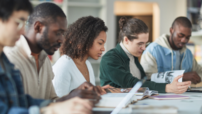 5 people sit together around a table, with one typing whilst the reminder read each form their own book.
