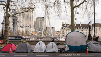 A row of tents pitched on the road, with the London Eye in the background.