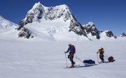 Two people in winter gear skii touring over a glacier while each dragging a sledge with them.