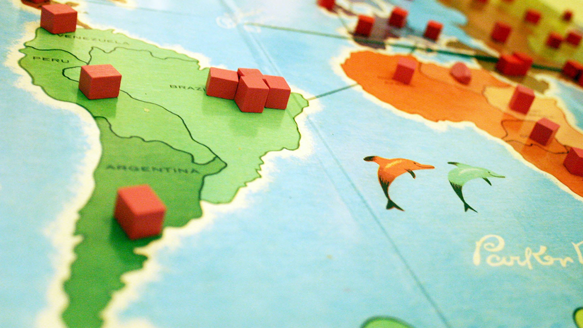 A close up of a board game on a table with small red cubes on a map of South America.