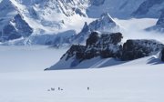 Group of people seen from a distance in the middle of a snowy mountainous landscape.