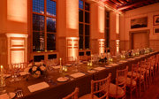 A formal candlelit banquet table in a grand main hall with warm orange uplighters. 