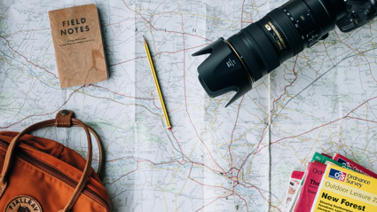 A backpack, books, notepad, pencil and digital camera sit on a map