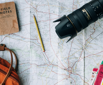 A backpack, books, notepad, pencil and digital camera sit on a map