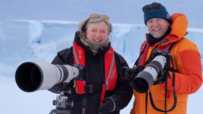 Sue Flood (left) and Ian Dawson (right) in the arctic, each holding a camera with a large lense.