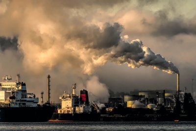 A river side view of industrial ships passing an industrial settlment. Smoke and smog fills the sky