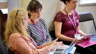 Three people sat with two people having a conversation while using a laptop.