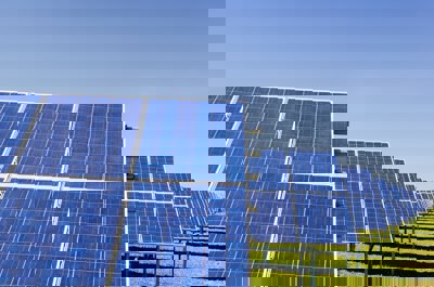 Blue solar panel sheets laid out in a green field. The sun is shining and the panels are casting a shadow on the grass