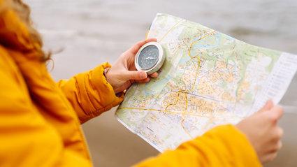 Close up of a person in a bright yellow coat holding a map and a compass.
