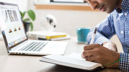 Person with laptop writing in a notebook.