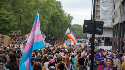 Crowd at a pride march holding transgender and rainbow flags with signs advocating for queer and trans liberation.