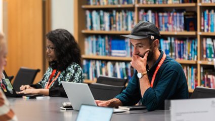 Two people using laptops while seated at a table in a library.