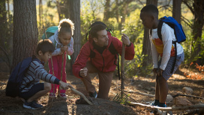 A teacher and three students examining soil in a forest.