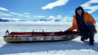 Preet Chandi in Antarctica next to sled with stickers of winning school logos.