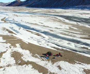 Streams of meandering glacial meltwater between areas of bare rock in the base of a valley. 