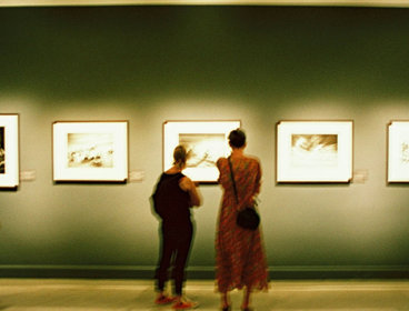 Two people looking at a picture in an exhibition gallery.