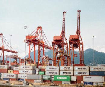 Shipping containers on a boat, with red cranes at the side ready to lift them on and off. 