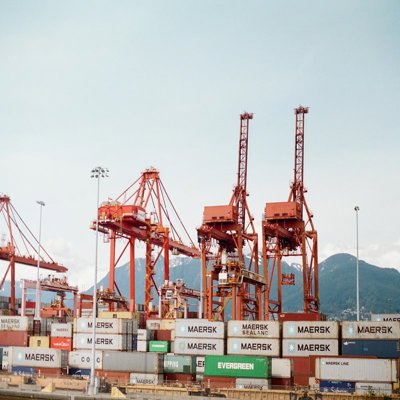 Shipping containers on a boat, with red cranes at the side ready to lift them on and off. 