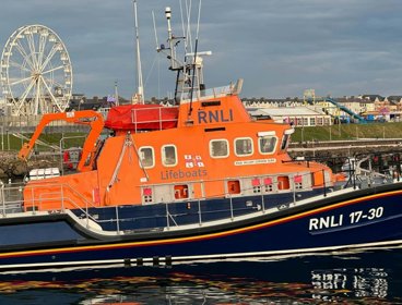 A large orange and blue boat labelled RNLI and lifeboat floating on top of water.