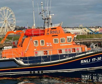 A large orange and blue boat labelled RNLI and lifeboat floating on top of water.