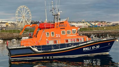 A large orange and blue boat labelled RNLI and lifeboat floating on top of water.