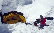 An expeditioner sitting in the snow and resting at a base camp.