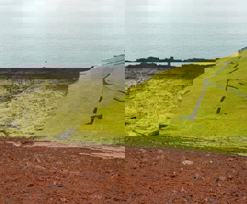 Aerial photo showing the contrast between volcanic stones and green grass right next to the sea.