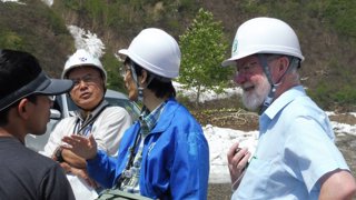 Three people in white hard hats and Murray Gray in a cap standing in natural landscape.