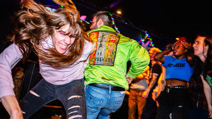 Two people dancing wildly at a crowded venue under colourful string lights.