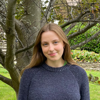 Poppy Burgess standing in front of a bare tree in a garden.