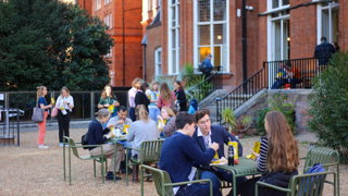 Explore attendees eating firepot food, sitting down on tables and chatting in the garden.