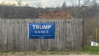 'Trump-Vance Make America great again 2024' election banner on a wooden fence in an agricultural setting.