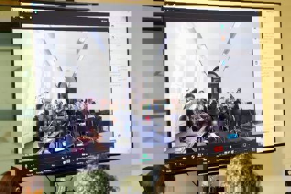 A digital screen showing a room with seated people