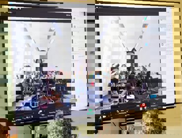 A digital screen showing a room with seated people