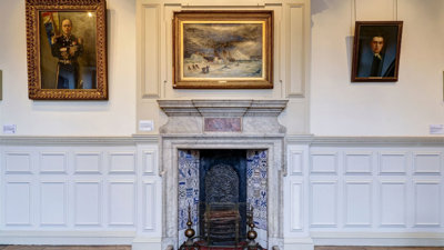 Wall in historic room featuring a fireplace and oil paintings hanging on the walls.