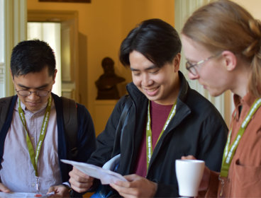 Three people talking at conference. They're looking at a sheet of paper.