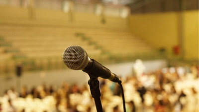 Close-up of a microphone on stand in front of a blurred out crowd of people.