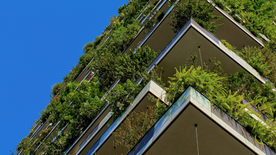 A tall apartment block features green foliage on every level and from both sides the building which are viewable.